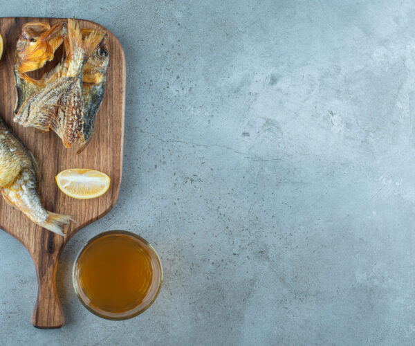 Fish, sliced lemon and a glass of beer on a board, on the marble background. High quality photo